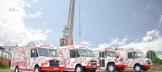 Vier Beefbusters Trucks stehen nebeneinander vor einem Kran