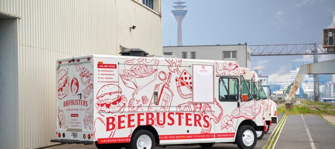 Beefbusters Trucks stehen in einer Reihe vor industriellem Hintergrund